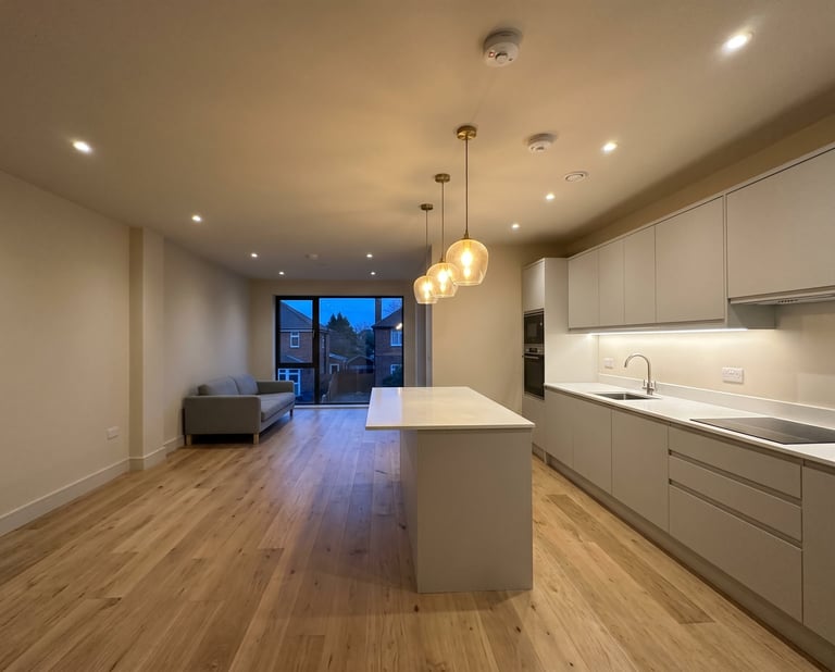 Modern open-plan kitchen and living room with white cabinetry, island counter, pendant lighting, and hardwood floors overlooking city lights.