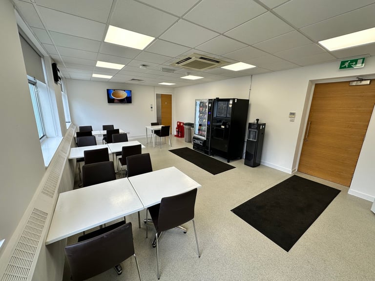 Modern office break room with white tables, black chairs, kitchen appliances, and computer monitors