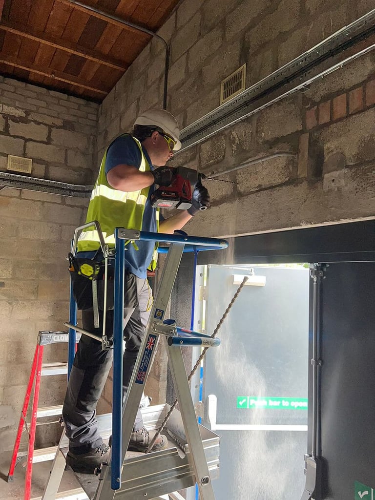 Construction worker in safety gear standing on a ladder performing maintenance work on interior walls in an unfinished room