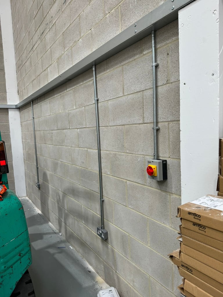 Concrete block wall with two vertical metal cables and a red and yellow emergency stop button mounted on the surface