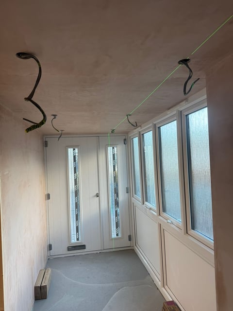 Unfinished room with white framed doors and windows, exposed ceiling with electrical wiring, concrete floor, and cable management hooks