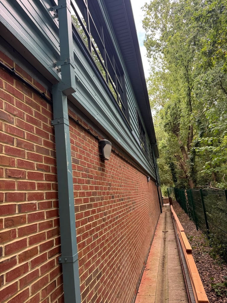Narrow brick passageway between a red brick building and ivy-covered wall with metal support beams
