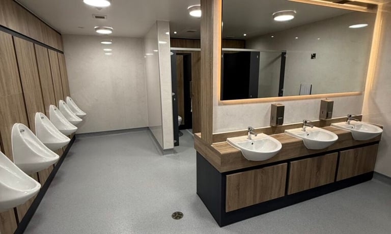 Modern public restroom with multiple white toilets on the left and a long vanity with dual sinks and large mirror on the right
